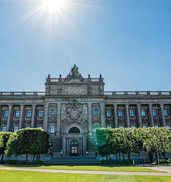 Front view of the Riksdag building with Swedish and EU flags on a sunny day.