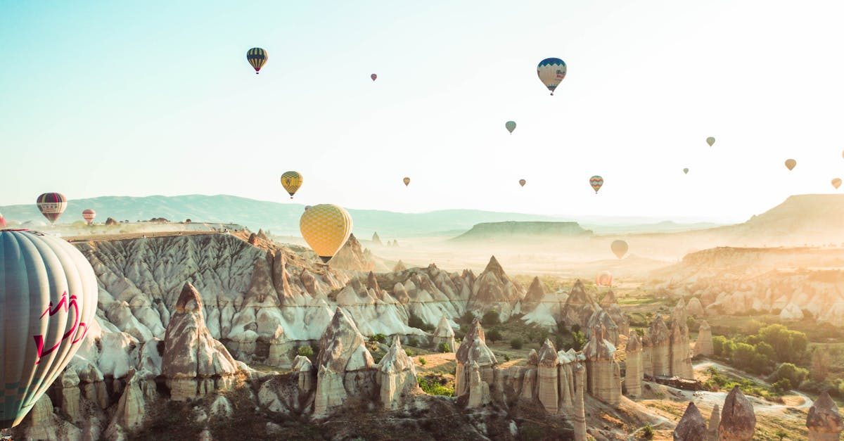 A stunning aerial view of hot air balloons floating over Cappadocia's rocky terrain during a sunny day.